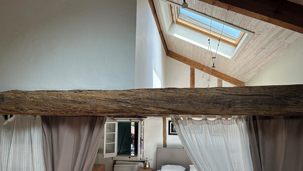 A bedroom with a sloped ceiling, a skylight, a bed with white bedding, and sheer curtains. - Basque farmhouse with swimming pool (Mouguerre)