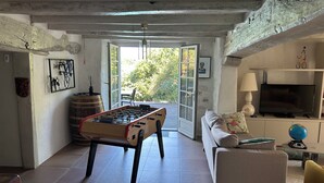 A spacious living room with a foosball table, a sofa, a television, and a large window offering a view of the outdoors. - Basque farmhouse with swimming pool (Mouguerre)
