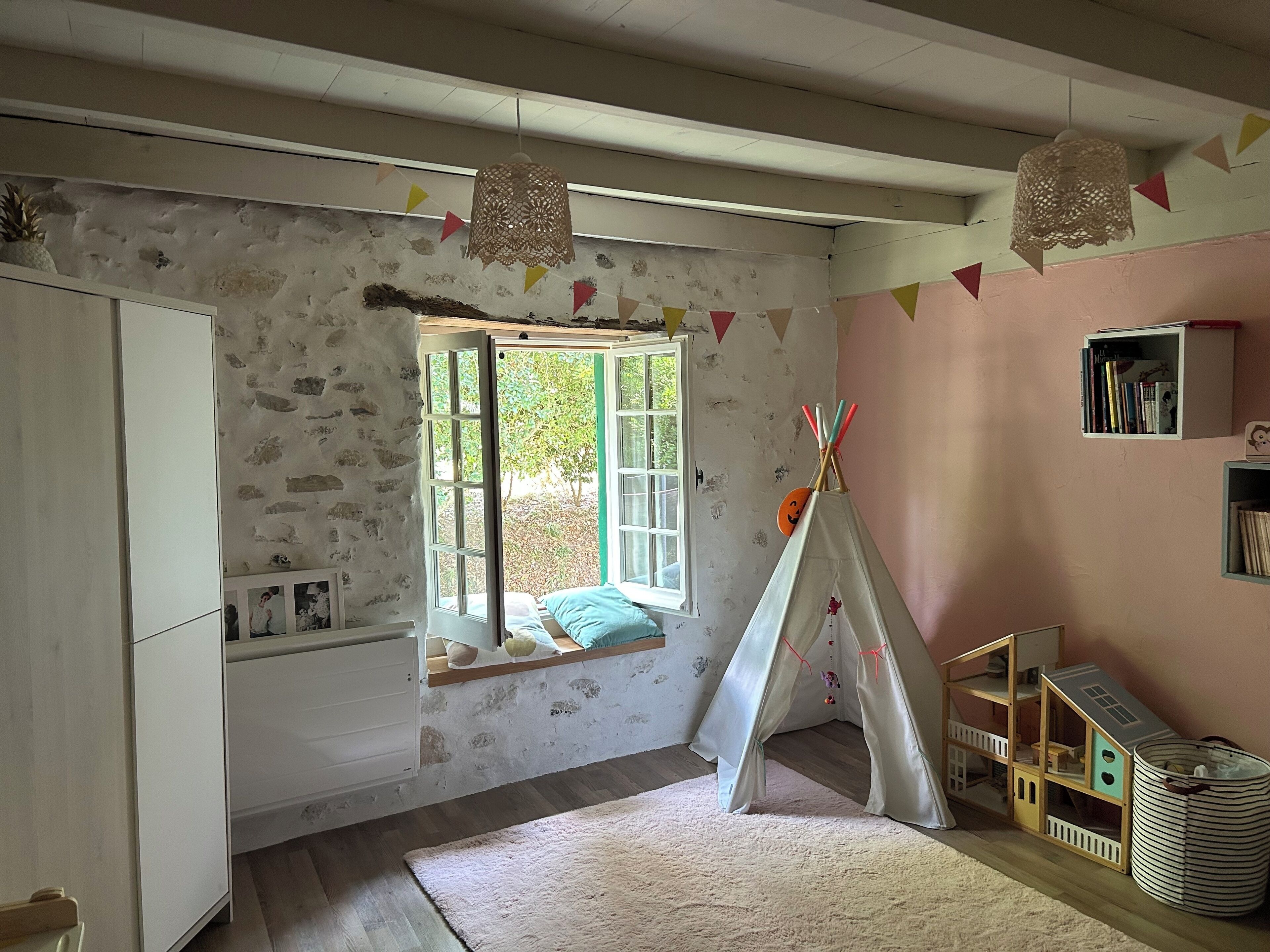 A child's bedroom with a window seat, a teepee, and a bookshelf.