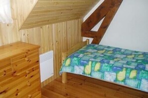 A small, wooden room with a sloped ceiling, a bed with a colorful quilt, and a wooden dresser with drawers.