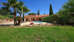 Ein Haus mit Swimmingpool, umgeben von einem gepflegten Garten mit Palmen und einer Steinmauer.