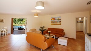 Ein geräumiges Wohnzimmer mit Sofa, Sessel und Couchtisch. An der Wand hängt ein Gemälde, und eine Tür führt in einen anderen Raum.