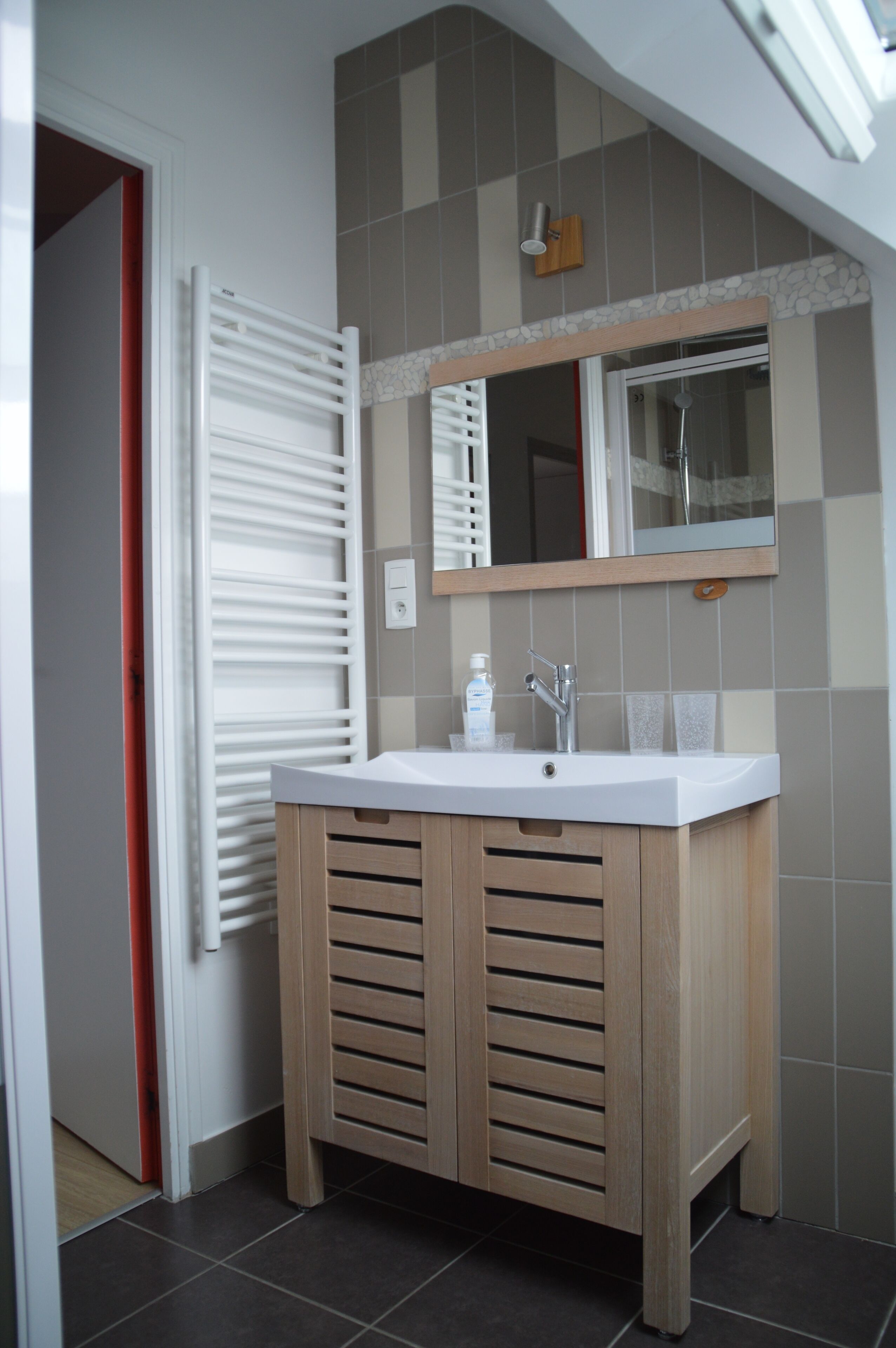 Une salle de bain avec un lavabo blanc, des meubles en bois, un miroir et un porte-serviettes.