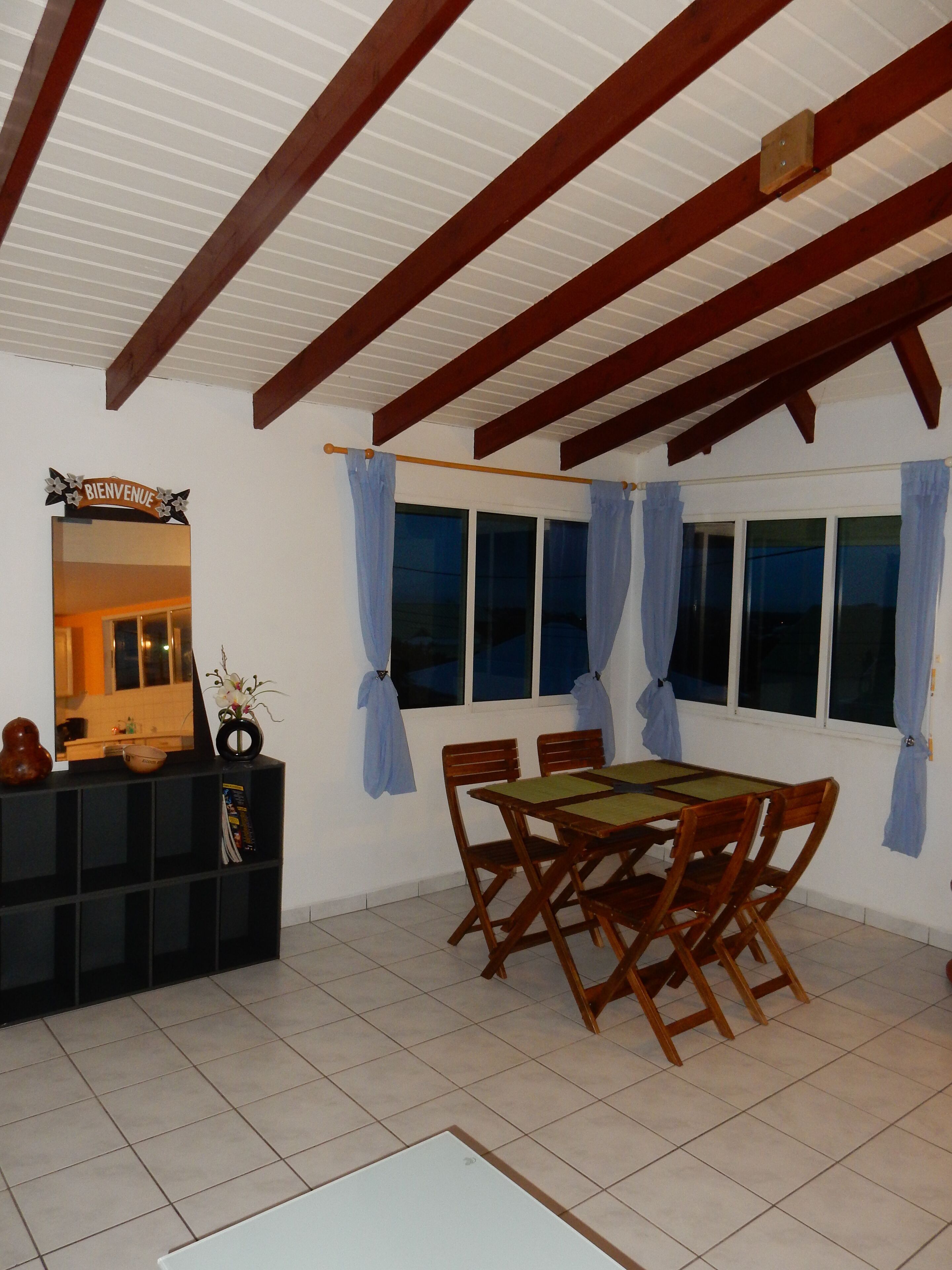 A dining area with a wooden table and chairs, a black console table with a mirror and decorative items, and a window with curtains.