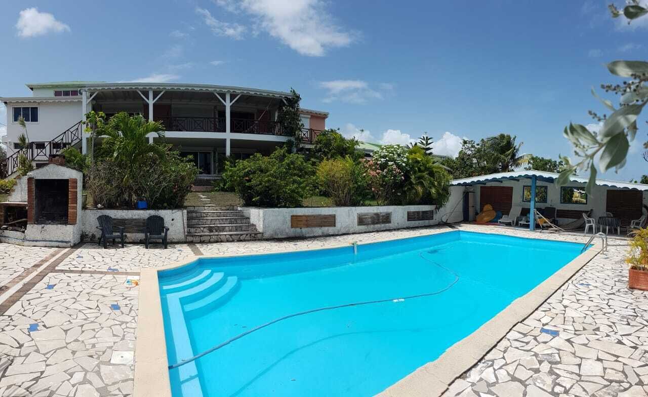 En swimmingpool med en terrasse belagt med sten, et overdækket siddeområde og en bygning med balkon i baggrunden.