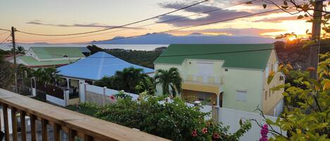 A residential area with houses, a wooden fence, and a view of the sea and mountains during sunset.