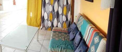 Una habitación con sofá, mesa de vidrio y cortina estampada.
