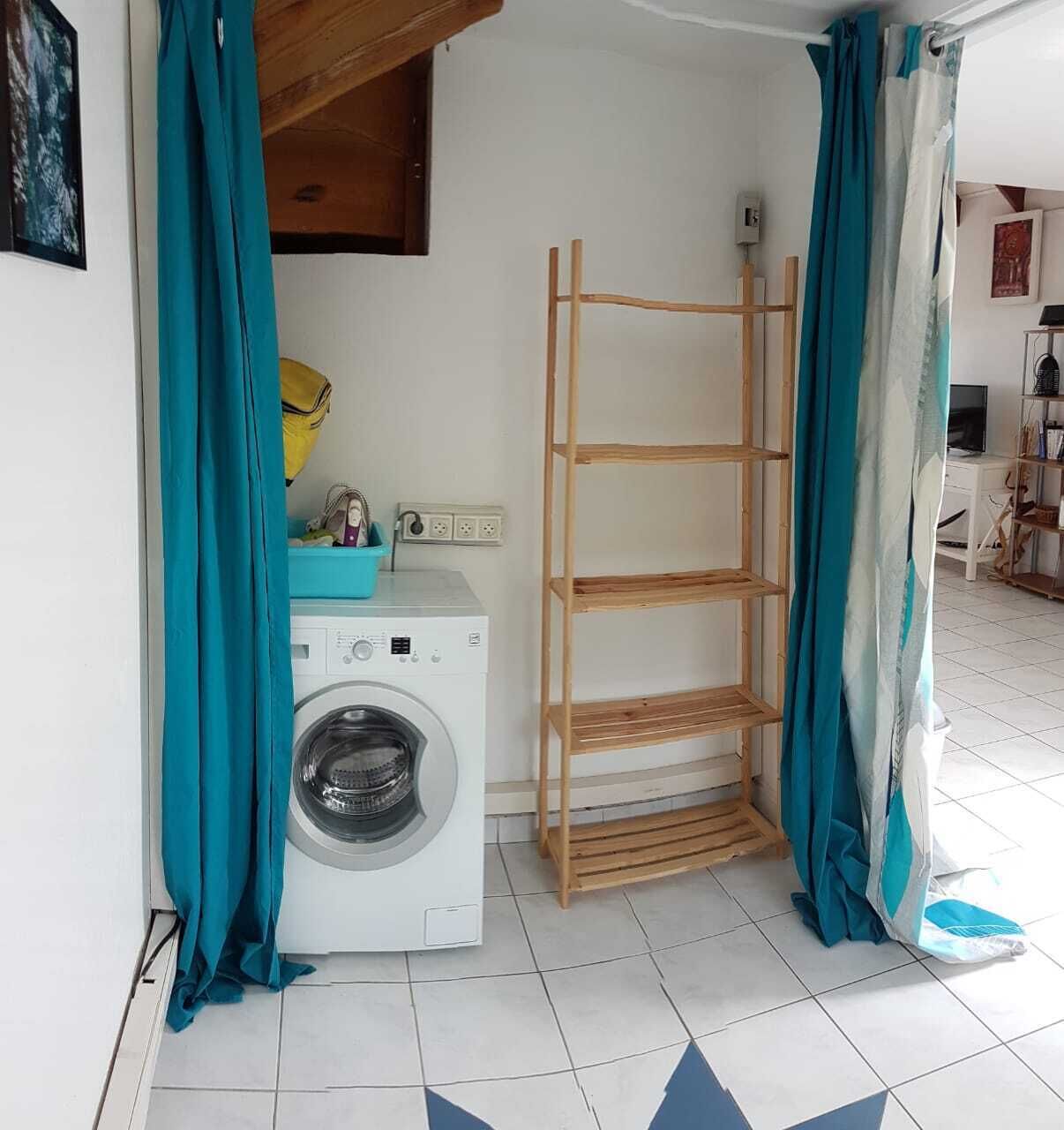 A laundry area with a washing machine, a drying rack, and a blue basin.