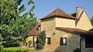 A stone building with a sloped roof and a chimney, surrounded by greenery. - House 12 Pers. Hamlet Dordogne (Saint-Martin-Des-Combes)