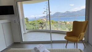 A room with a large window offering a view of the sea and mountains. There is a yellow armchair and a rolled-up towel on a woven mat. - CALVI, MAGNIFICENT CONTEMPORARY VILLA WITH SEA VIEW AND HEATED POOL  (Calvi)