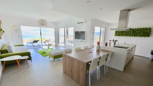 A modern kitchen with a dining area, a TV, and a view of the ocean. - CALVI, MAGNIFICENT CONTEMPORARY VILLA WITH SEA VIEW AND HEATED POOL  (Calvi)
