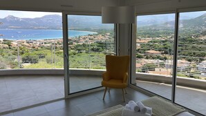 A modern room with large floor-to-ceiling windows, a yellow chair, and a view of a coastal landscape. - CALVI, MAGNIFICENT CONTEMPORARY VILLA WITH SEA VIEW AND HEATED POOL  (Calvi)