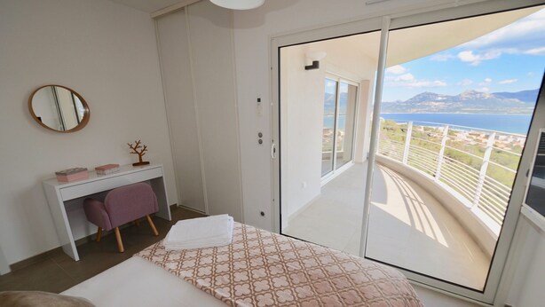 A bedroom with a bed, a desk, a chair, and a large sliding glass door leading to a balcony with a view of the sea and mountains. - CALVI, MAGNIFICENT CONTEMPORARY VILLA WITH SEA VIEW AND HEATED POOL  (Calvi)