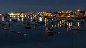 Un puerto deportivo al anochecer, con barcos amarrados y luces de la ciudad reflejándose en el agua.