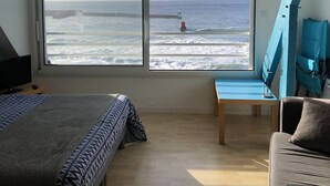 A bedroom with a large window overlooking the ocean, a bed, a desk, and a chair. - A studio located in a house directly on the beach in a stunning maritime site (Guilvinec)