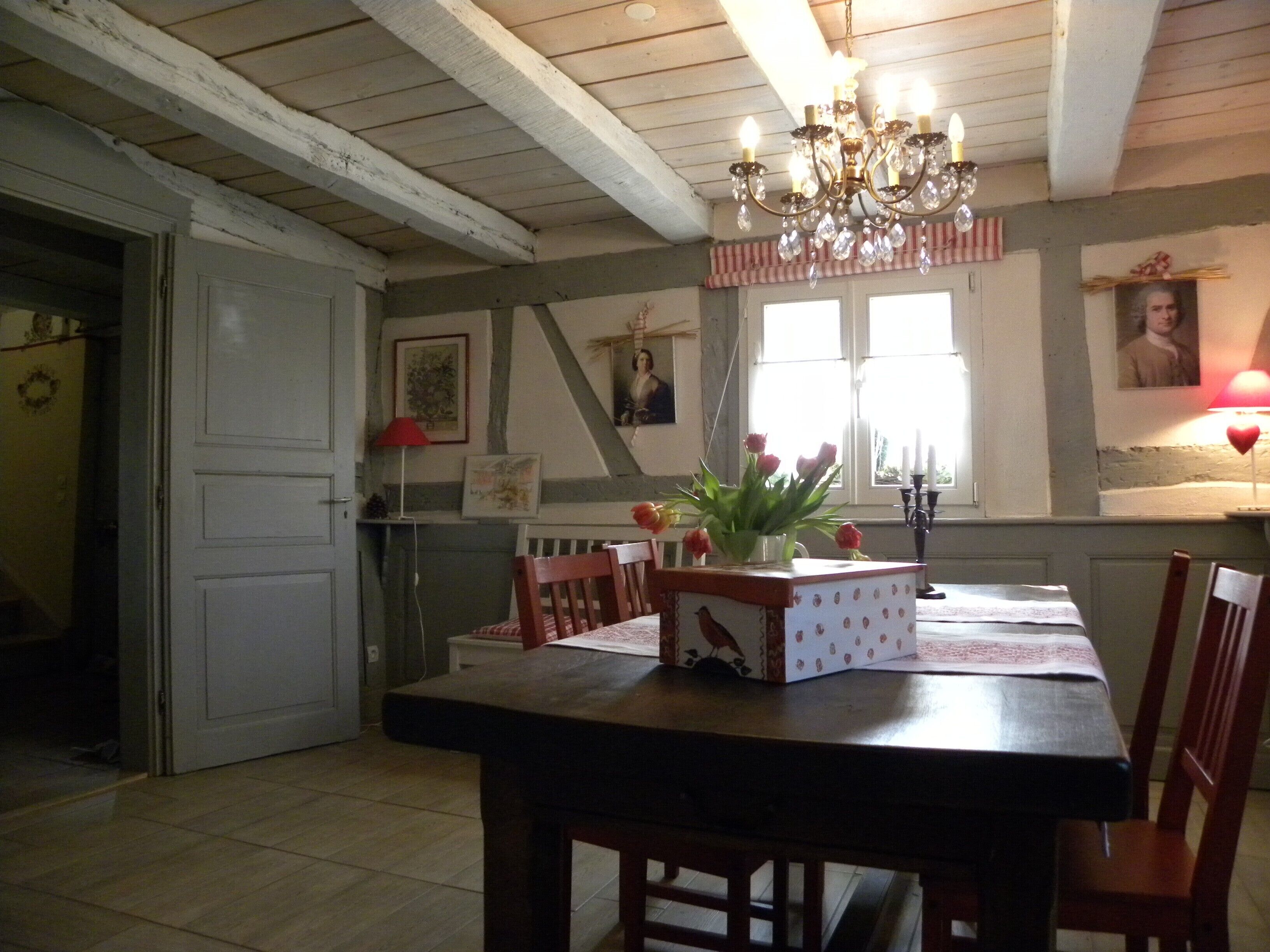 Ein Essbereich mit einem Holztisch, Stühlen, einer Chandelier und einem Fenster mit Vorhängen.
