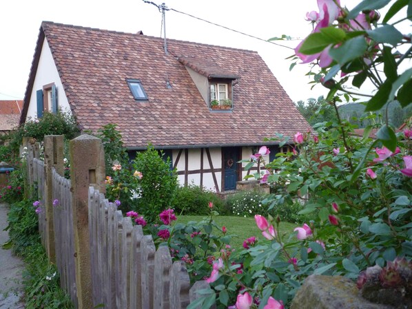 Una casa tradicional de entramado de madera con techo inclinado, una valla de madera y un jardín lleno de flores.