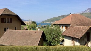 A traditional chalet-style building with a sloped roof, surrounded by well-maintained hedges and a clear view of a lake and mountains in the distance.