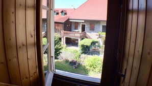 A wooden-framed window with a view of a house with a red roof and a balcony.