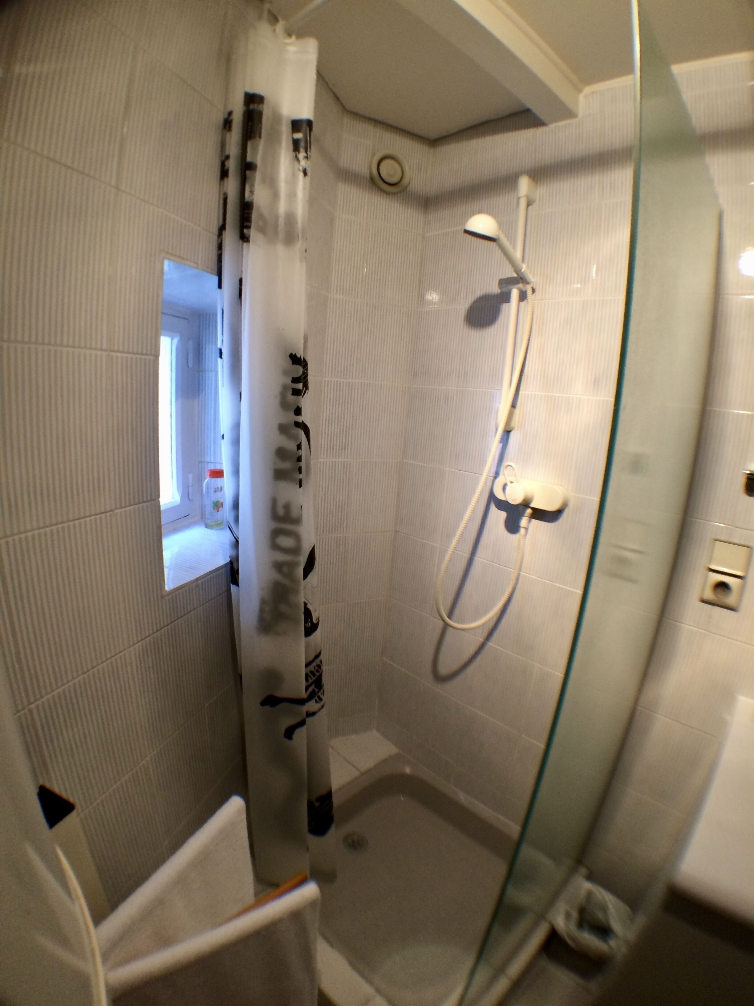 A small, enclosed glass shower stall with a handheld showerhead and a wall-mounted faucet.
