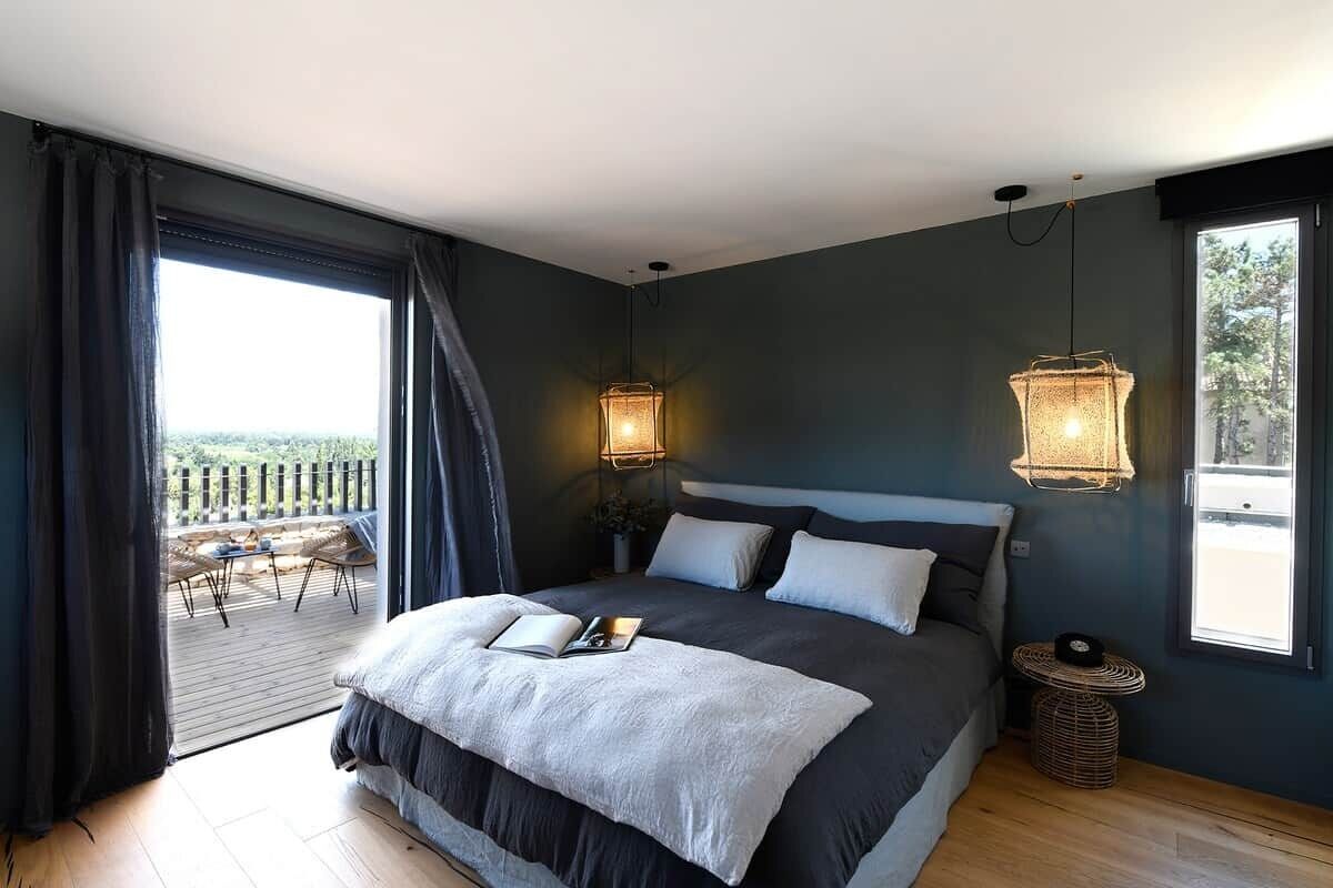 Une chambre avec un grand lit, deux lampes de chevet, une vue sur l’extérieur grâce à une porte coulissante donnant sur un espace extérieur, et une petite table ronde.