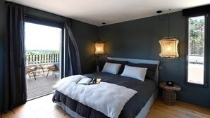 A bedroom with a large bed, two bedside lamps, a view through a sliding door to an outdoor area, and a small round table. - Les Loges en Provence - Villa "Ventoux (Villeneuve-lès-Avignon)