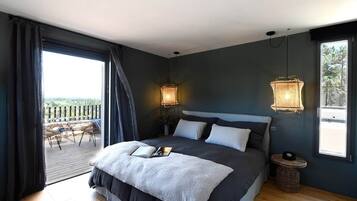 Une chambre avec un grand lit, deux lampes de chevet, une vue sur l’extérieur grâce à une porte coulissante donnant sur un espace extérieur, et une petite table ronde.