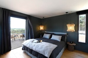 A bedroom with a large bed, two bedside lamps, a view through a sliding door to an outdoor area, and a small round table. - Les Loges en Provence - Villa "Ventoux (Villeneuve-lès-Avignon)