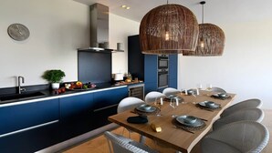 A modern kitchen with blue cabinetry, a dining area with a wooden table set for six, and two large wicker pendant lights. - Les Loges en Provence - Villa "Ventoux (Villeneuve-lès-Avignon)
