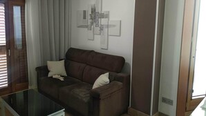 Ein Wohnzimmer mit einem braunen Sofa, einem Glastisch und einem an der Wand befestigten abstrakten Kunstwerk.