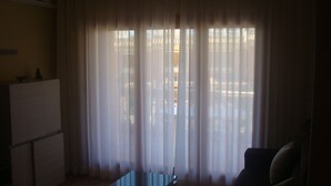 Ein Zimmer mit einem großen Fenster, das mit transparenten Vorhängen drapiert ist, einem kleinen Tisch und einem Sofa.