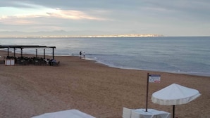 Ein Strand mit einer überdachten Sitzgelegenheit und einem Schild, das eine Schwimmzone von 12 Metern kennzeichnet.