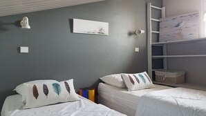 A bedroom with two beds, each with white bedding and decorative pillows. There is a white wall with a framed picture and a white shelf with a basket. - Holiday rental 5 people ideally located in St Martin de Ré (Saint-Martin-De-Ré)