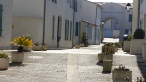 A narrow cobblestone street lined with white buildings featuring arched doorways and blue shutters. - Holiday rental 5 people ideally located in St Martin de Ré (Saint-Martin-De-Ré)