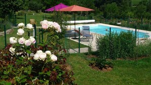 Piscina com área cercada, rodeada por vegetação e um jardim de rosas.