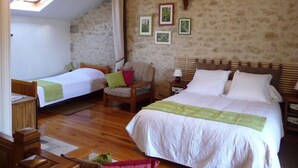 Um quarto acolhedor com duas camas de solteiro, uma cadeira de madeira, uma mesinha e uma parede de pedra.