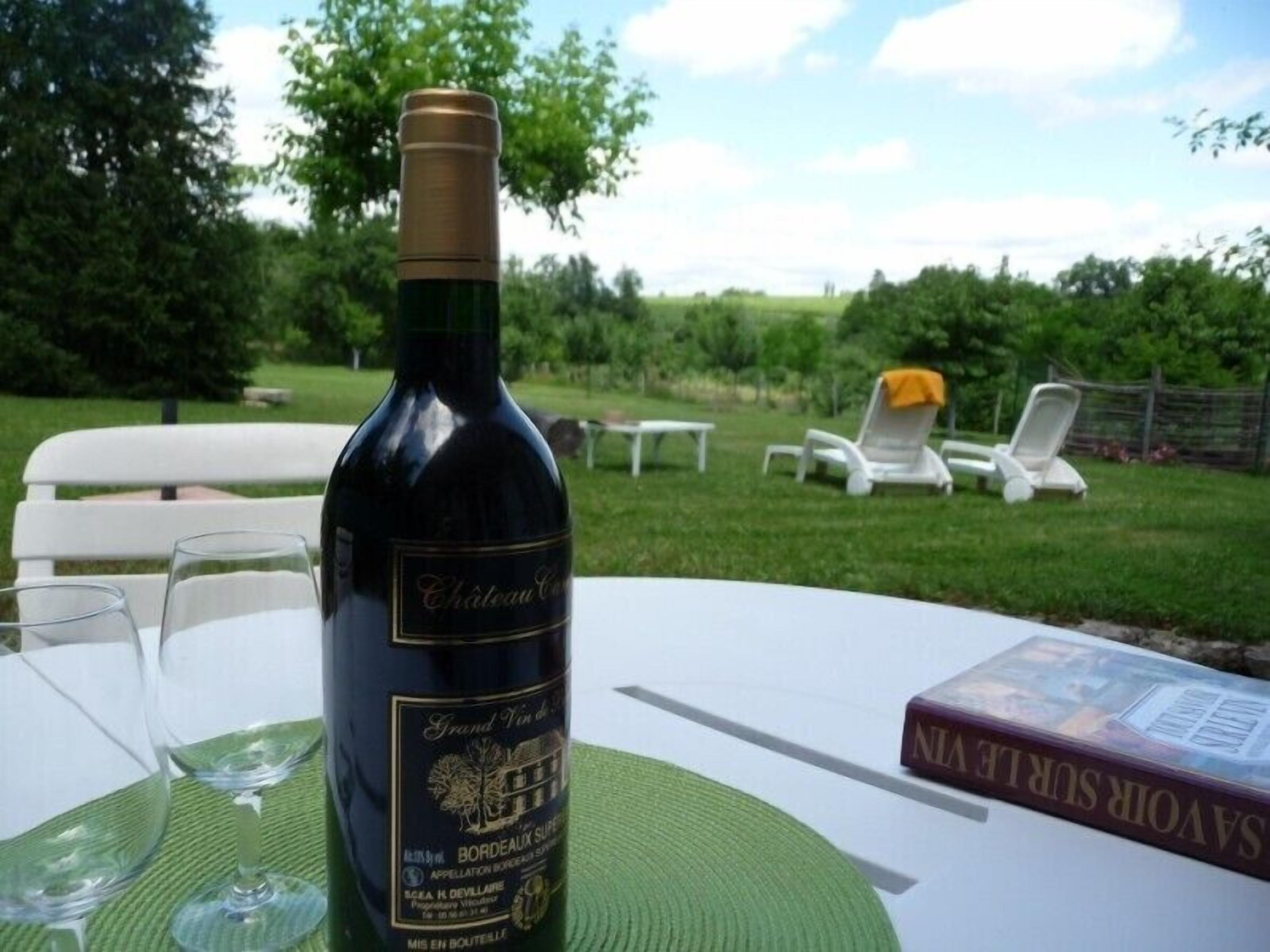 A bottle of Chateau Grand Vin de Bordeaux on a table with two wine glasses and a book titled "SAVOR SURRENDER".