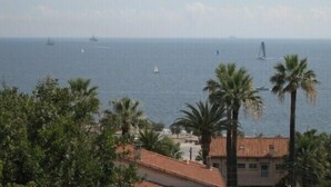 A coastal view with a clear sky, palm trees, and a building with a red-tiled roof. - For six people, 1st floor of villa, sea view apartment of 80m2 (Toulon)