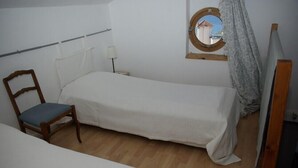 A single bed with a wooden frame, a chair with a blue cushion, a small table with a lamp, and a round mirror on the wall. - For six people, 1st floor of villa, sea view apartment of 80m2 (Toulon)