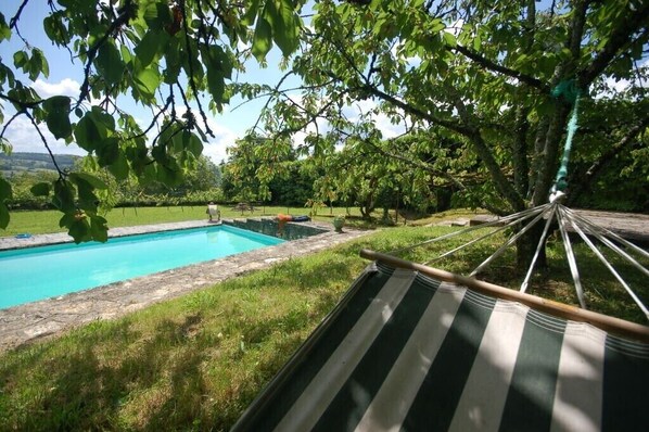 A hammock overlooking a swimming pool with a grassy area and trees in the background. - Family house in Saint-Robert (Corrèze) (Saint-Robert)