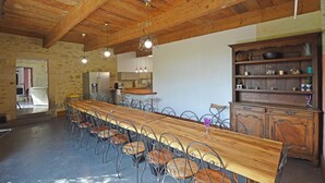 Un comedor amplio con una larga mesa de madera y sillas metálicas, un aparador de madera con estantes y una cocina al fondo.