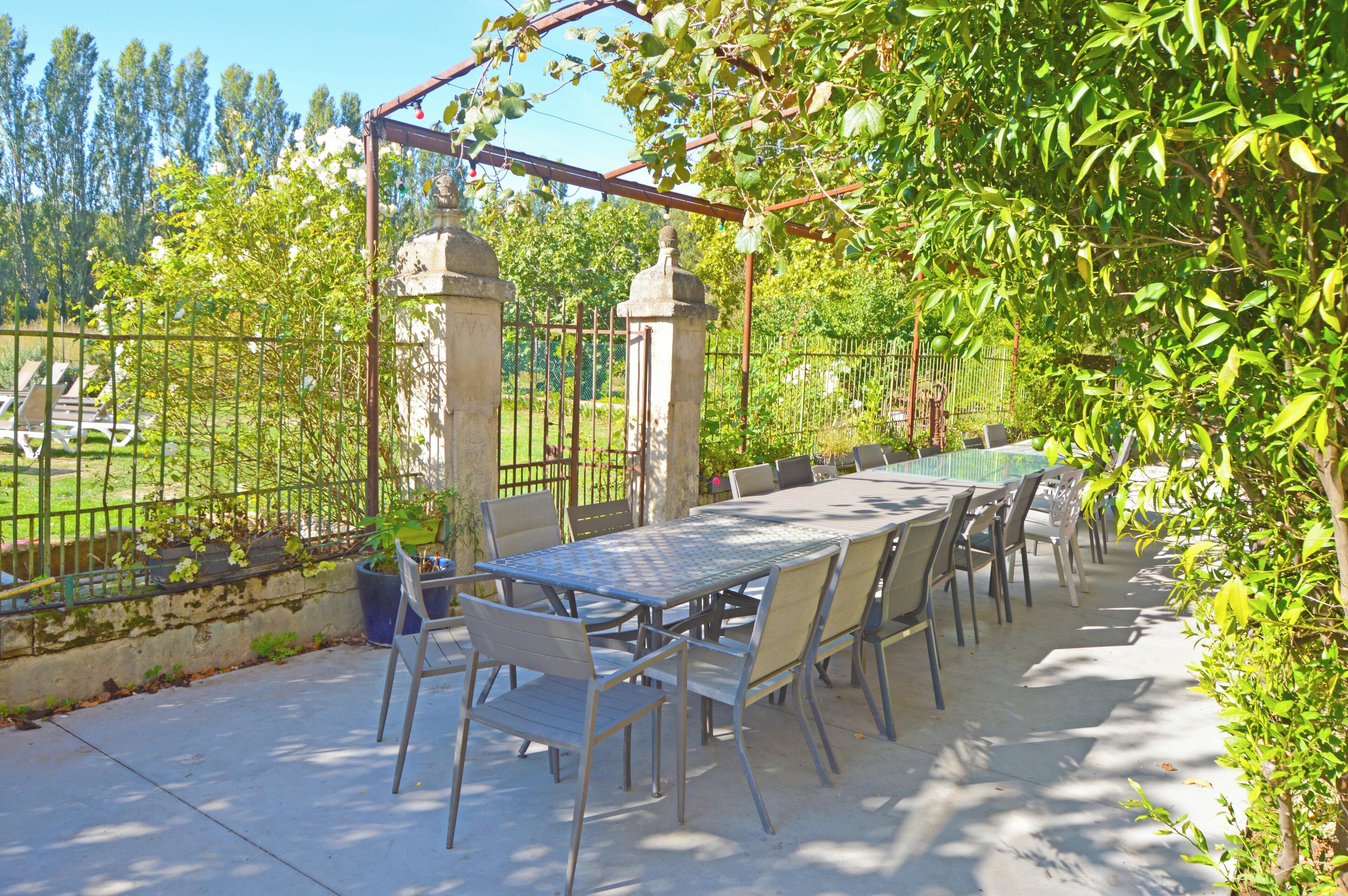 An outdoor patio with a table and chairs, surrounded by a metal fence and greenery.