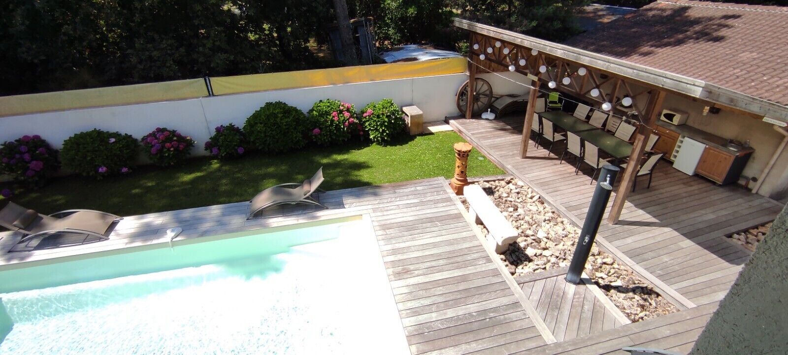 Un jardin avec une piscine, une terrasse en bois et un espace barbecue.
