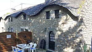 Un bâtiment en pierre avec un toit en tuiles, une porte en bois et une table avec des chaises à l’extérieur.