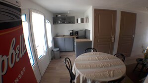 Une cuisine de taille réduite comprenant un coin repas, une poubelle et un réfrigérateur.