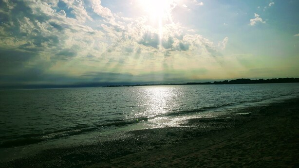 Une plage où la lumière du soleil se reflète sur l’eau et où l’on peut voir des nuages dans le ciel.