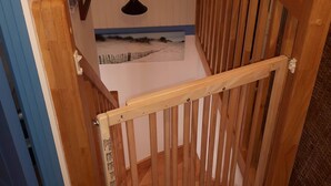 Une porte en bois donne sur une pièce où l’on trouve une porte blanche, une petite table et un tableau représentant une scène de plage accroché au mur.