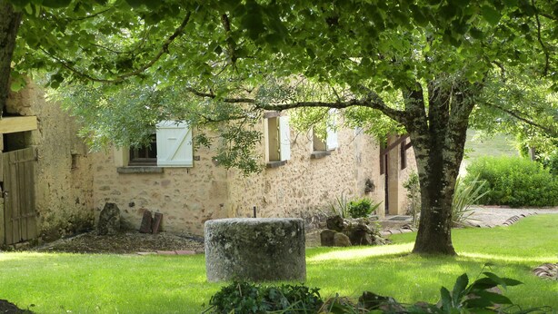 A rustic stone building with a wooden door, a stone bench, and a well-maintained lawn.