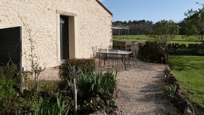 A rustic stone building with a gravel patio, outdoor seating, and a view of a green field.
