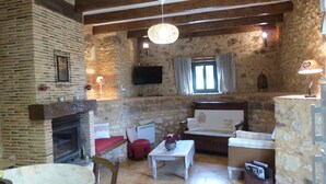 A rustic living room with exposed stone walls, a fireplace, wooden beams, a television, and a cozy seating area.